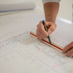Ein Mitarbeiter der SSN Gebäudetechnik zeichnet auf einem Bauplan mit einem Lineal und Stift eine Linie